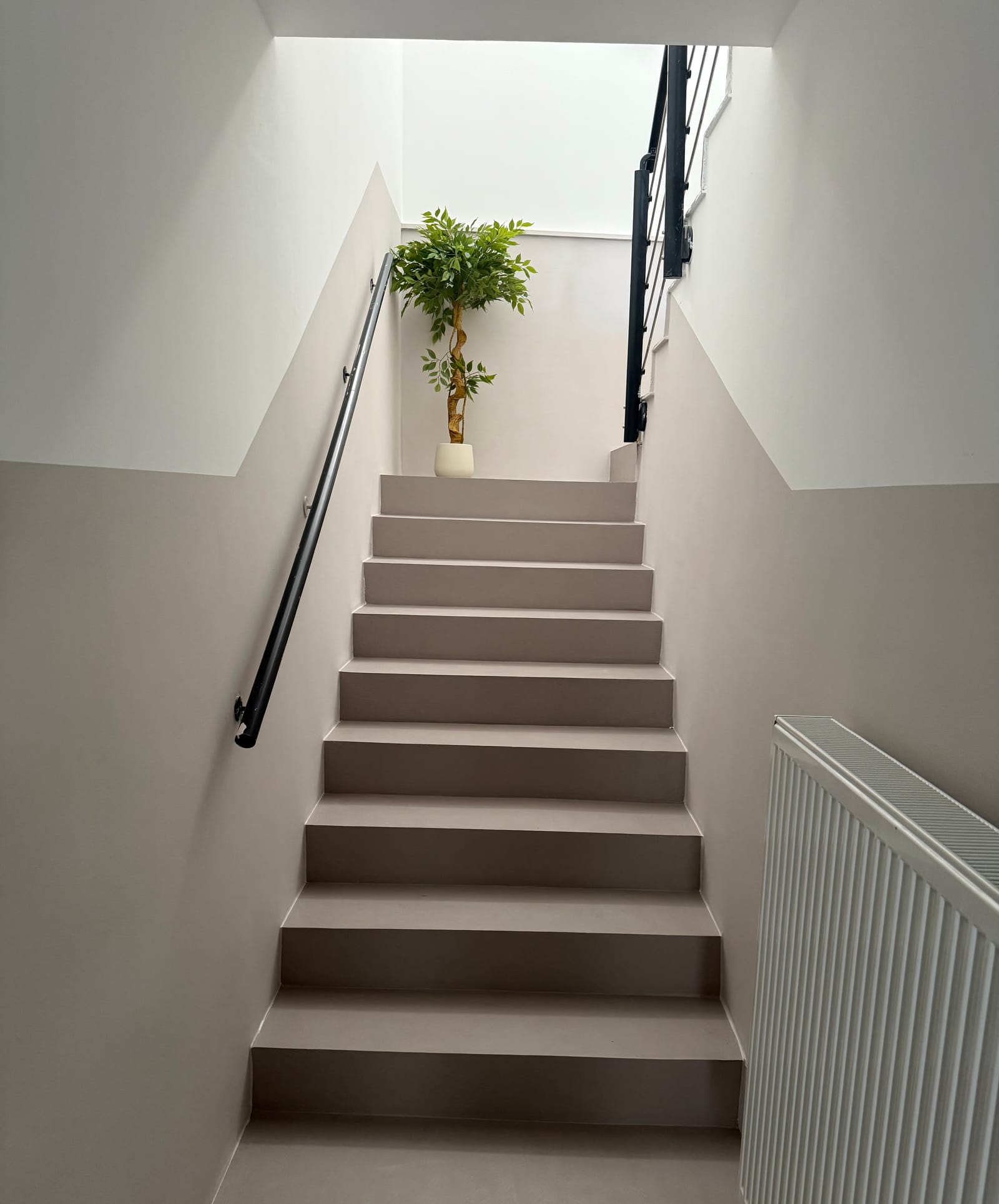 Treppenaufgang fugenlos in Mikrozement Taupe-Beige mit beschichteten Wänden und schwarzem Handlauf