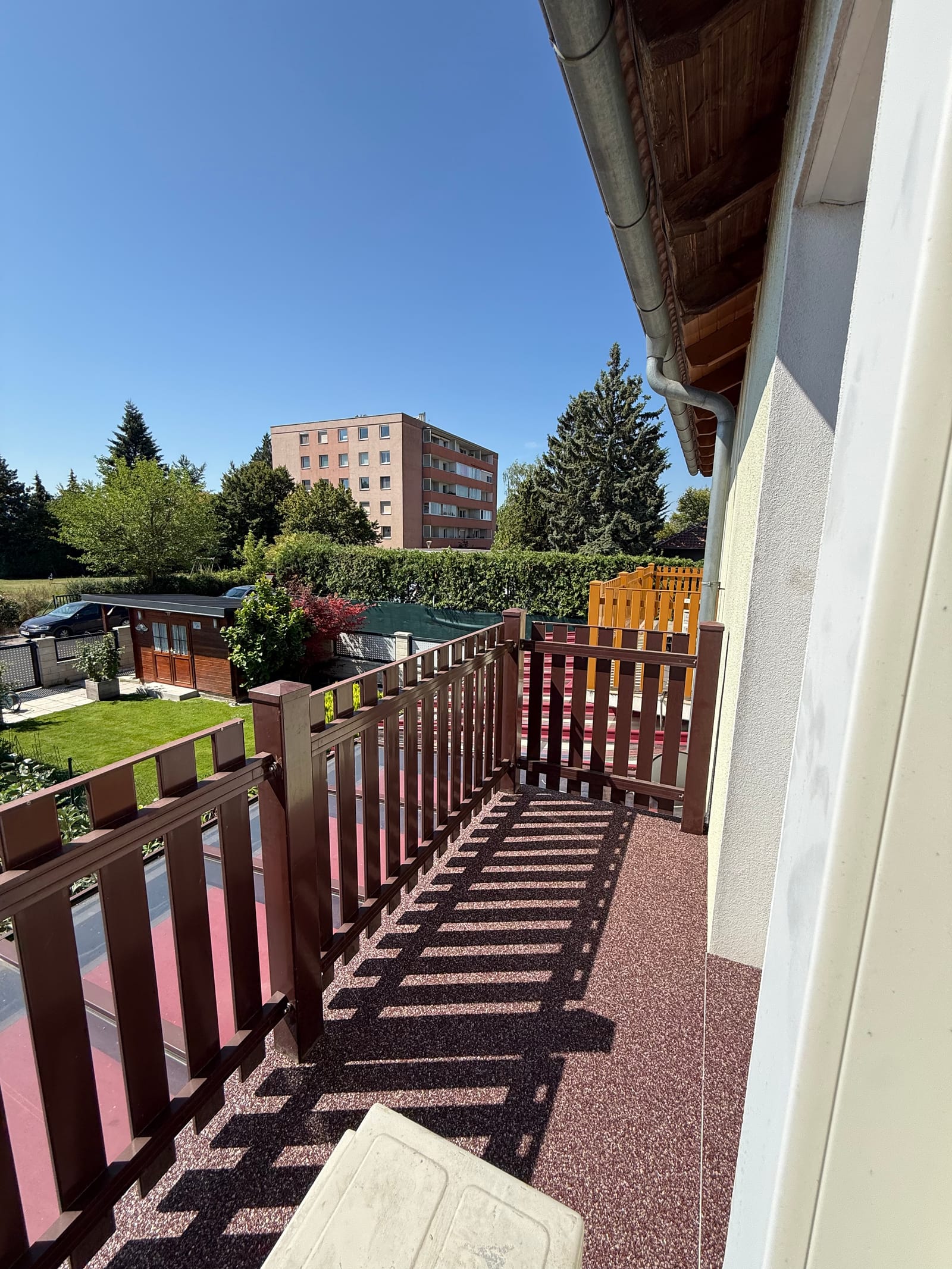 Balkon mit Natursteinteppich in meliertem Terracotta-Rot, Holzgeländer und Blick über den Garten