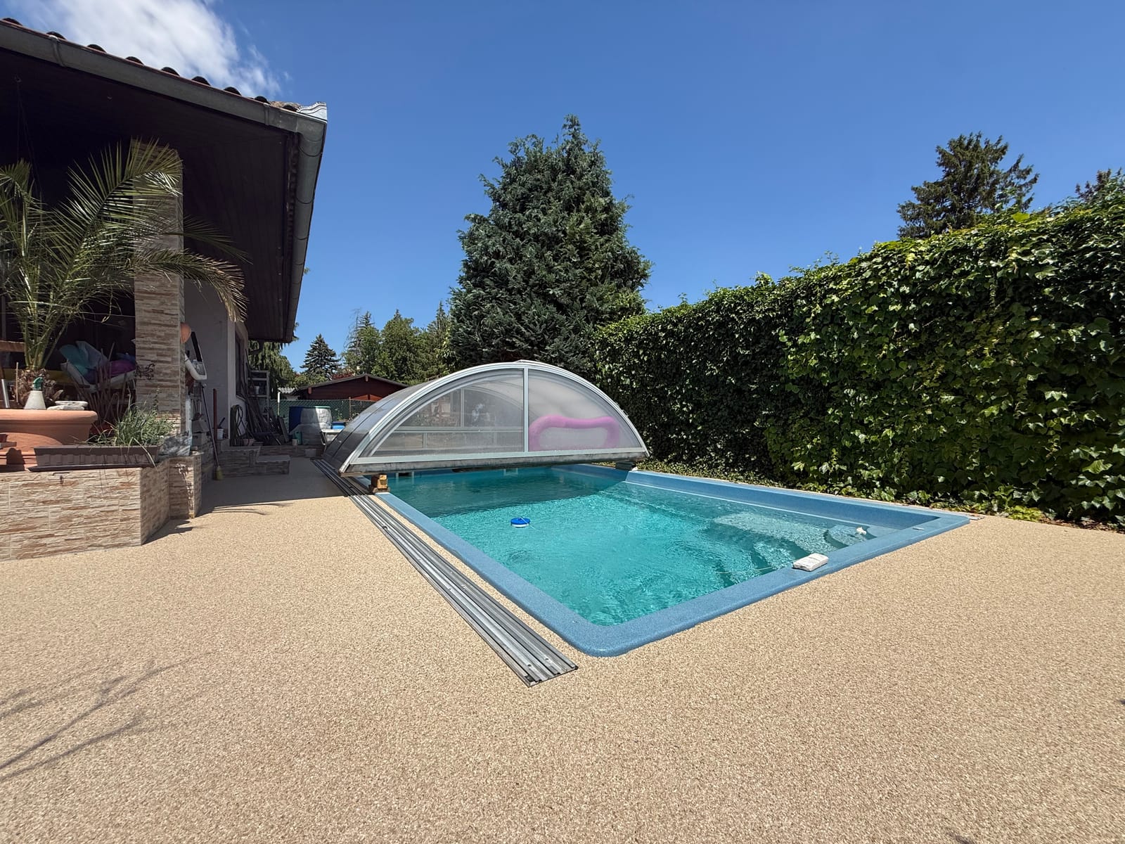 Natursteinteppich rund um den Pool in Beige mit Pool-Überdachung und Heckeneinfassung