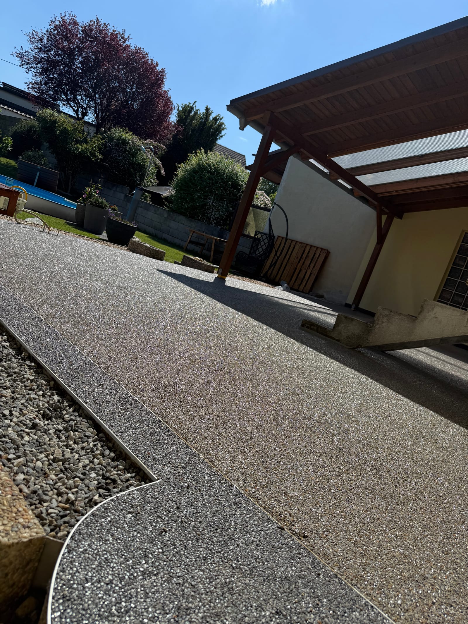 Natursteinteppich-Terrasse in Beige neben überdachtem Carport mit Poolbereich und Garten